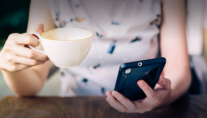 A woman is drinking from a coffee mug and reading from her phone.