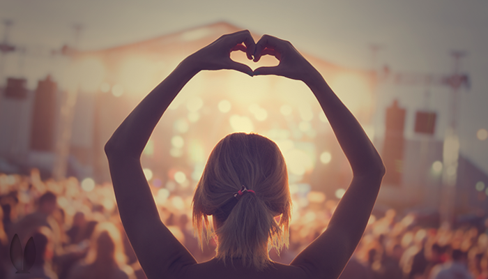 A girl making a heart with her hands in front of a crowd.