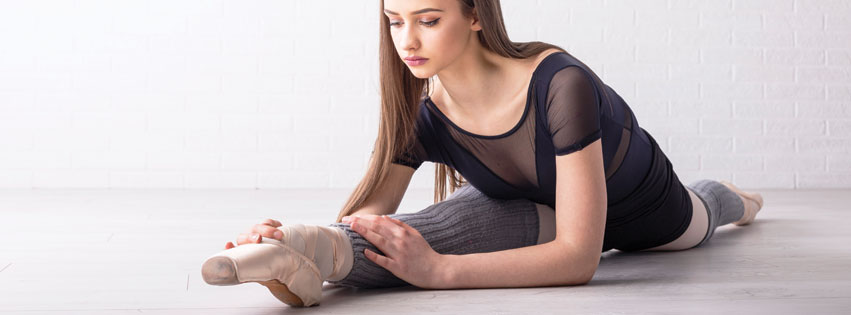 Ballerina stretching using a foot stretcher before exercising.