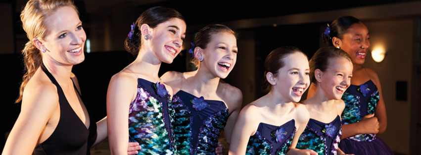 Costumed dancers are laughing together after their dance recital.