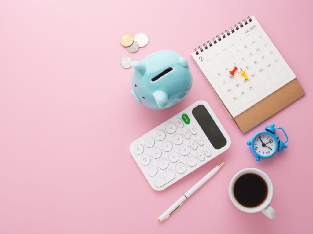 A piggy bank, calculator, calendar, pen, clock and a cup of coffee like flat on a pink background.